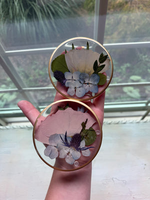 Two round resin coasters with preserved pink, blue and white flowers, held in a hand.