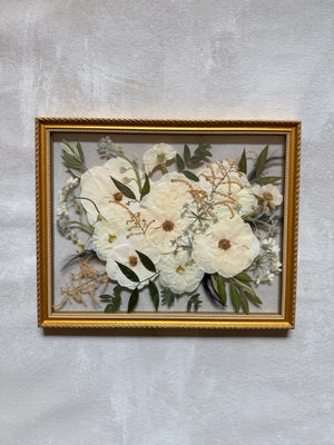 Pressed cream and white flowers with greenery in a gold floating frame.
