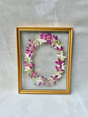 Pressed pink and white flowers arranged in a wreath, in a gold floating frame.
