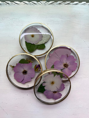 Four round resin coasters with silver rims and preserved lavender and purple flowers.