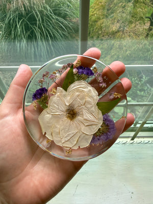 Round resin coaster with a preserved white flower and purple accents, held in a hand.