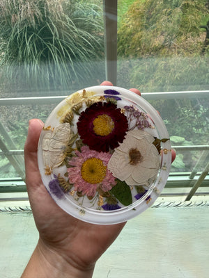Round resin ring dish with preserved white, burgundy and pink flowers, held in a hand.