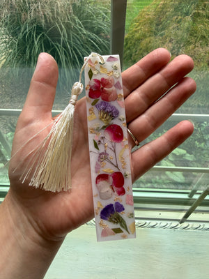 Resin bookmark with preserved red, pink and purple flowers and a cream tassel, held in a hand.