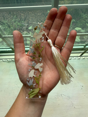 Resin bookmark with preserved cream and pink flowers, greenery and a cream tassel, held in a hand.