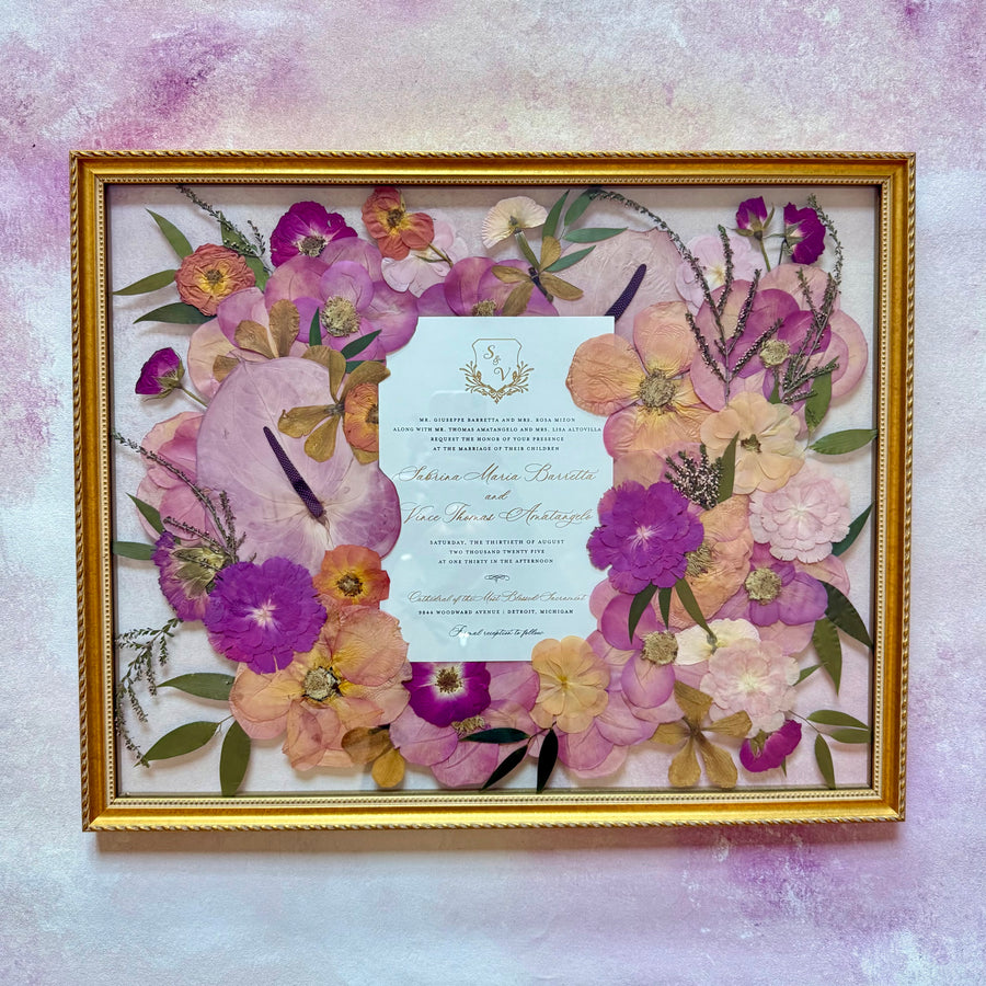 Wedding invitation placed at the center of a pressed flower design, surrounded by pink, peach and magenta flowers.