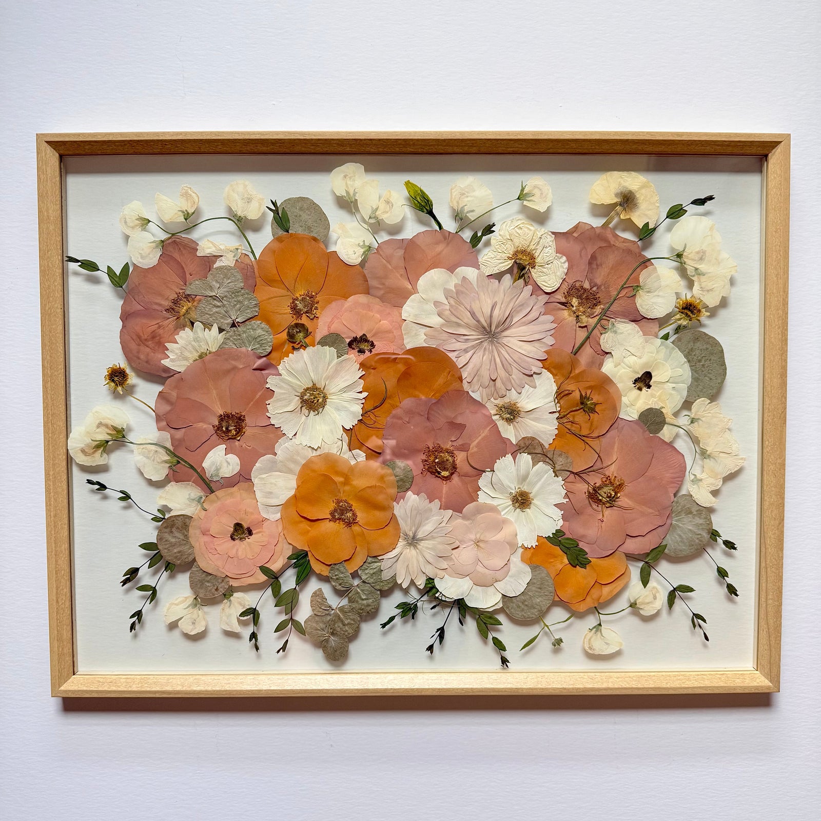 Pressed peach, orange, blush and cream flowers in a natural wood floating frame.