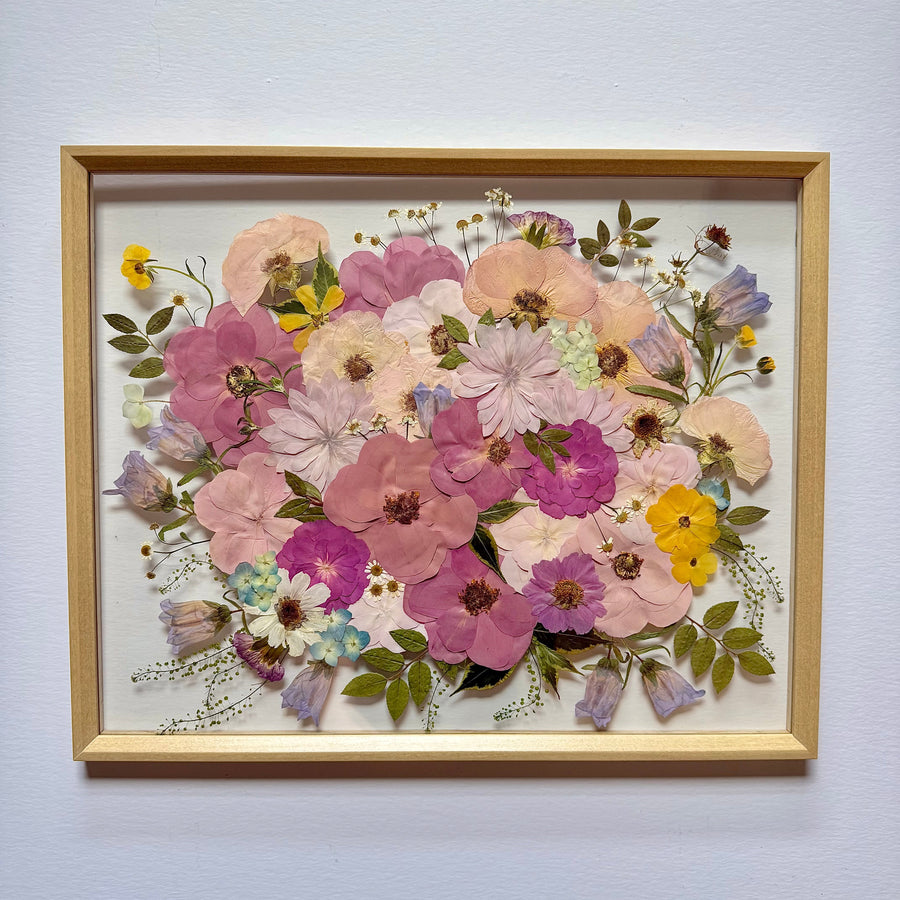 Pressed pink, magenta, peach and yellow flowers in a bouquet design, in a natural wood floating frame.
