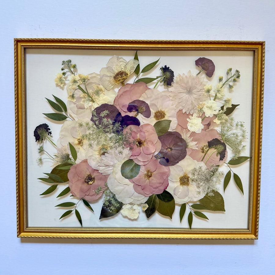 Pressed blush, mauve, purple and white flowers with greenery in an ornate gold frame.