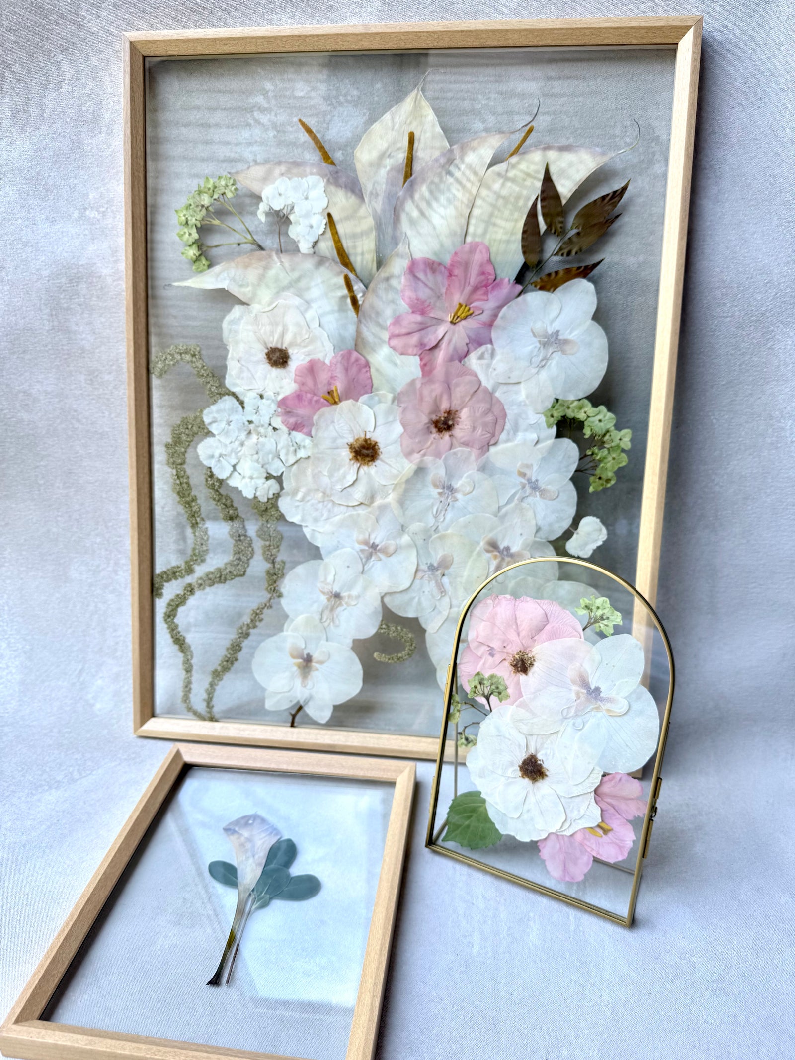 Pressed white and pink flowers in a natural wood floating frame, with a boutonniere frame and a small arch keepsake.