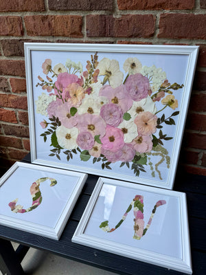 Pressed pink, lavender and white flowers in a white floating frame, with two small monogram letter frames.