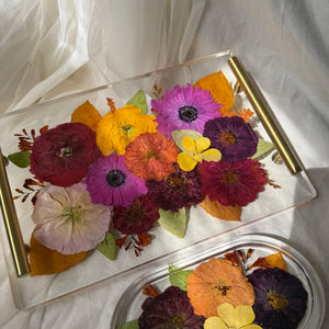 Clear resin rectangle tray with gold handles and preserved red, purple, orange and yellow flowers.