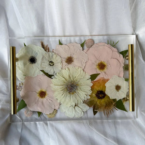 Clear resin rectangle tray with gold handles and preserved pink and white flowers.