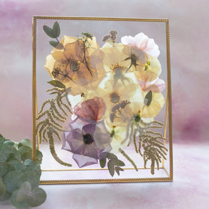 Gold freestanding glass frame with pressed cream, peach and lavender flowers and ferns.